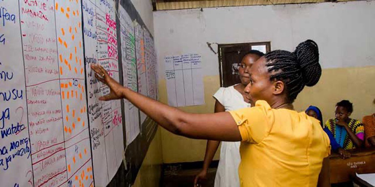 Two participants look at handwritten data and insights on large notepad pages in a classroom.