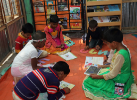 Seven children reading books and tablets on the floor in a library