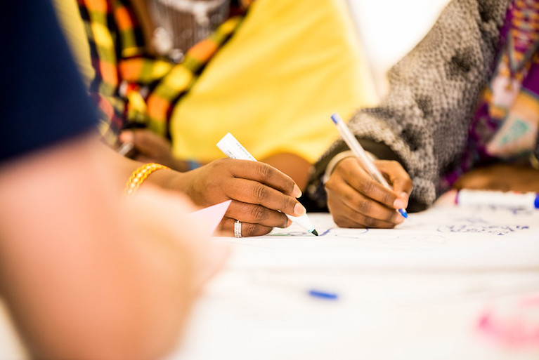 A photo of two people's hands holding pens and writing on a piece of paper