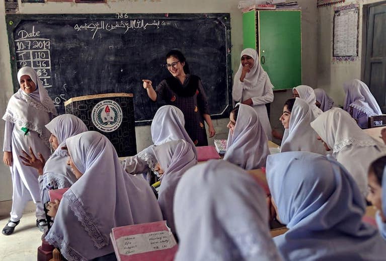 A woman stands at the front of a classroom speaking to a group of young women