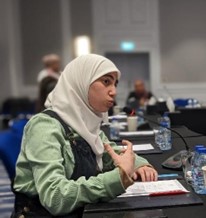 Young woman wearing a Hijab at a table speaking into microphone
