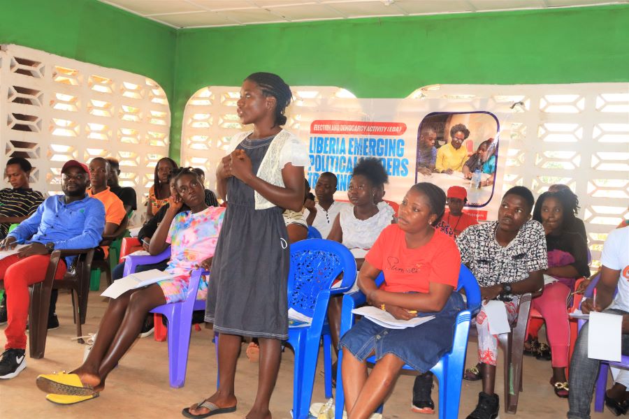 Youth Leaders participating in the Liberia Emerging Political Leaders Training. A young female leader is standing and making a presentation while her colleagues observe her.