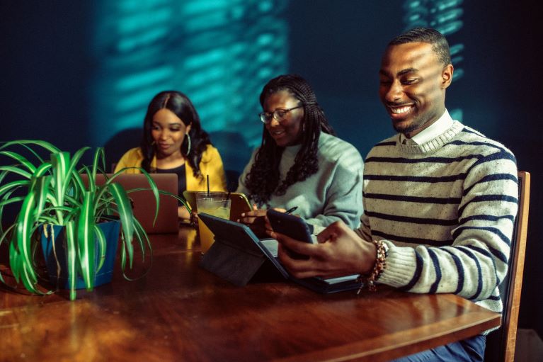 Three young people sit at a desk with computers