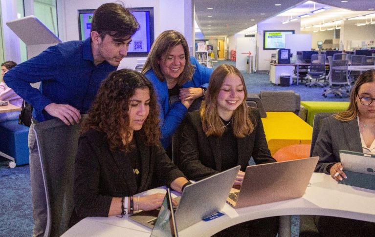 Group of students huddle around a laptop