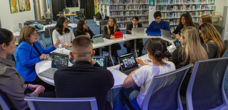 Young students sit around a table with video call on laptops
