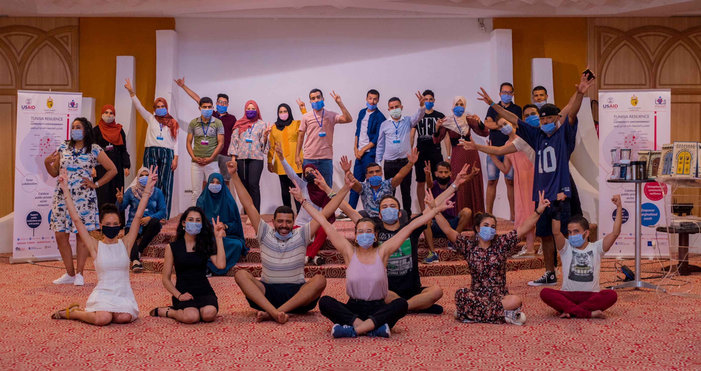 Photo of youth posing for a photo at a conference with their hands in the air and masks on their faces.