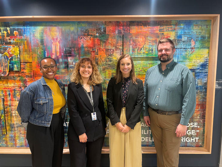 Four people smiling for a photo in front of a wall at their CEE host organization