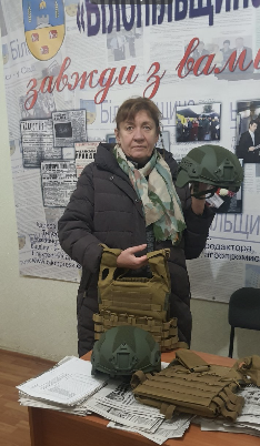 Photo of Natalia Kalinichenko in an office, holding up a protective vest and helmet 