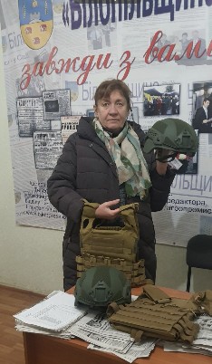 Photo of Natalia Kalinichenko in an office, holding up a protective vest and helmet
