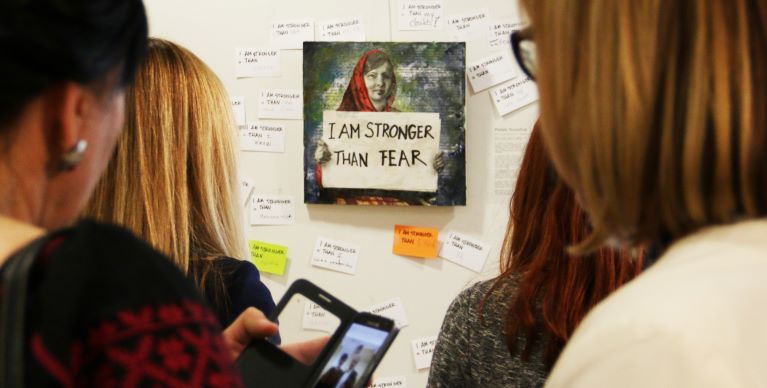 People viewing art of Malala with sign that says "I am stronger than Fear"