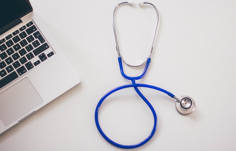 Photo of a laptop and a stethoscope on a table.