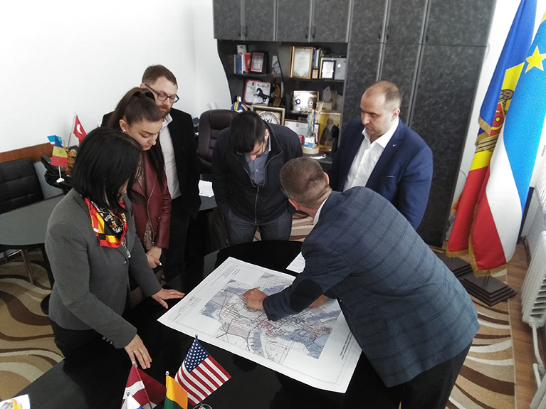 Photo of a vice-mayor in Comrat. He's leaning over a map and explaining to a small group how he uses geospatial information.