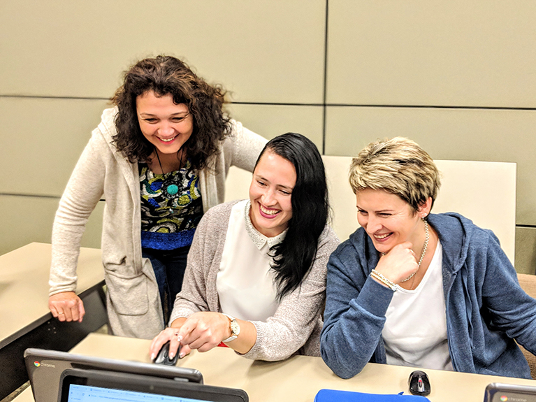 Photo of three teachers smiling and looking at a laptop.