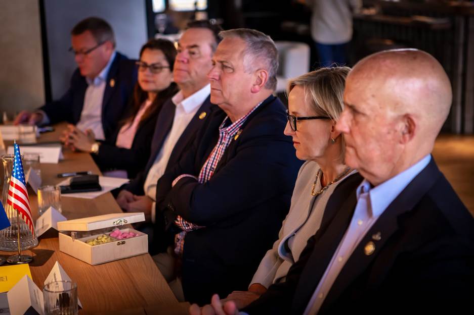 Photograph of a group of six people seated at a conference table, appearing focused and engaged in a formal meeting or discussion.