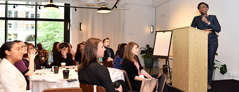 Speaker at a podium and participants listening at their tables.