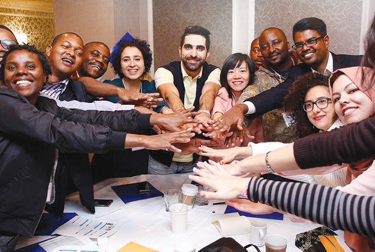 Photo of participants smiling and putting their hands in the middle of a conference table.
