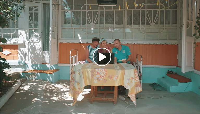 Three people sitting in front of a laptop at a patio table.