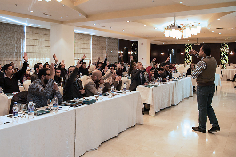 A facilitator interacting with dozens of participants in a conference room.