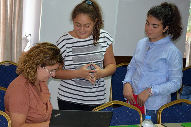 Two journalism students with a mentor, who is reviewing their work at a table