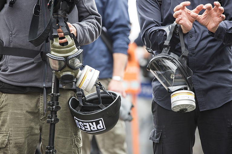 Two journalists with gas masks and helmets.
