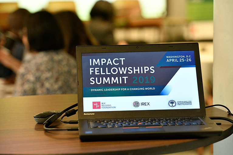 A laptop on a table at a conference. The laptop's screen says Impact Fellowships Summit 2019.