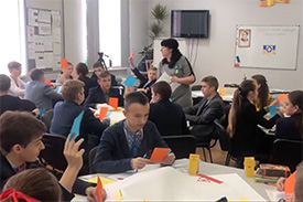 A teacher and students in a classroom in Ukraine. The students are doing a media literacy exercise with orange and blue pieces of paper.