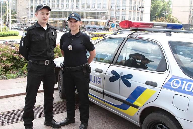 Two Ukrainian police officers standing next to a police car