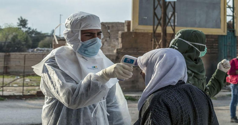 Photo of two health workers and a patient who are standing outside. One of the health workers is taking the patient's temperature.