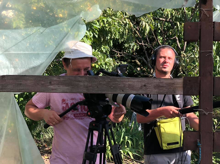 Photo of a person using a video camera and a person holding a microphone boom pole on the set of the Moldovan sitcom Italia Patria Nostra.