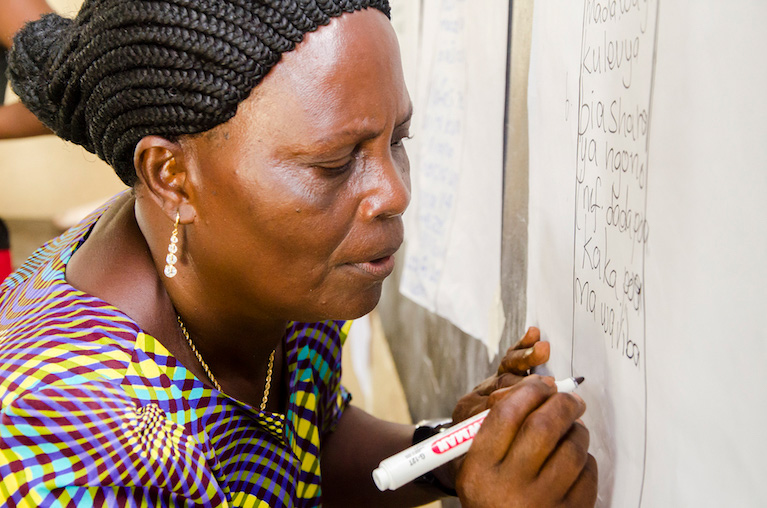 Photo of a woman writing on a page of notepad paper at a chalkboard.