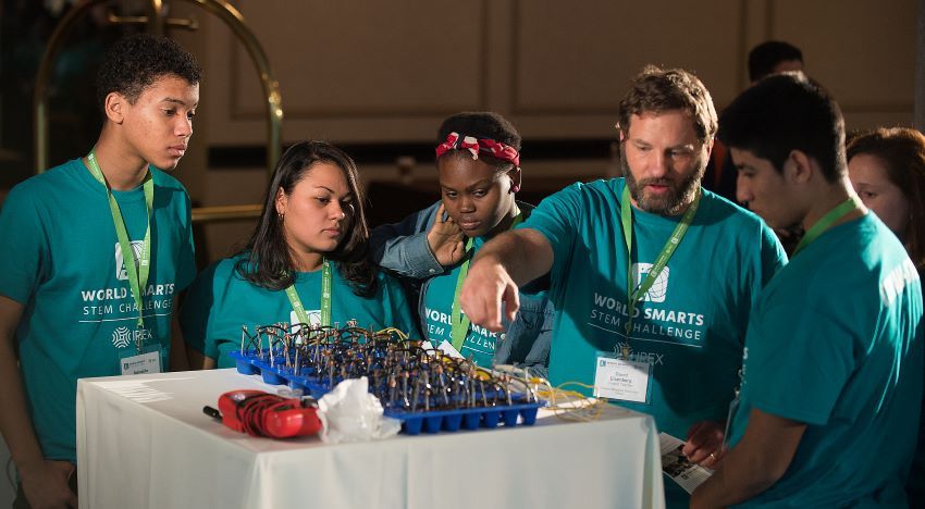 Teacher and students standing in front of table conducting an experiment 