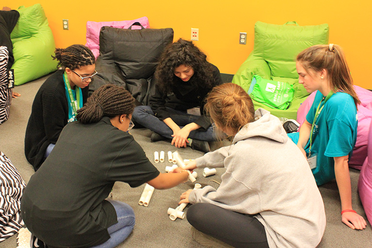 Five young people collaborate on an activity while sitting in a circle on the floor.