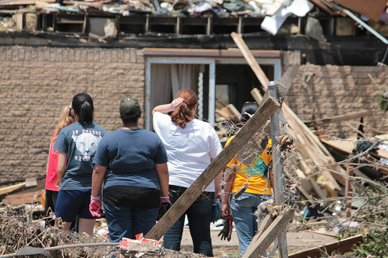 Photo of five people standing in the wreckage of a building after a disaster.
