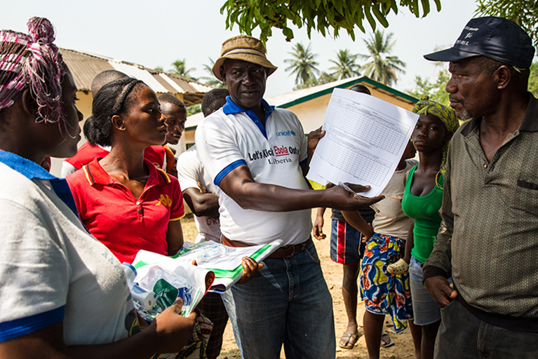 Photo of a group of Liberian citizens who are standing in a semicircle. One person is holding up a sheet of paper that shows a blank grid.