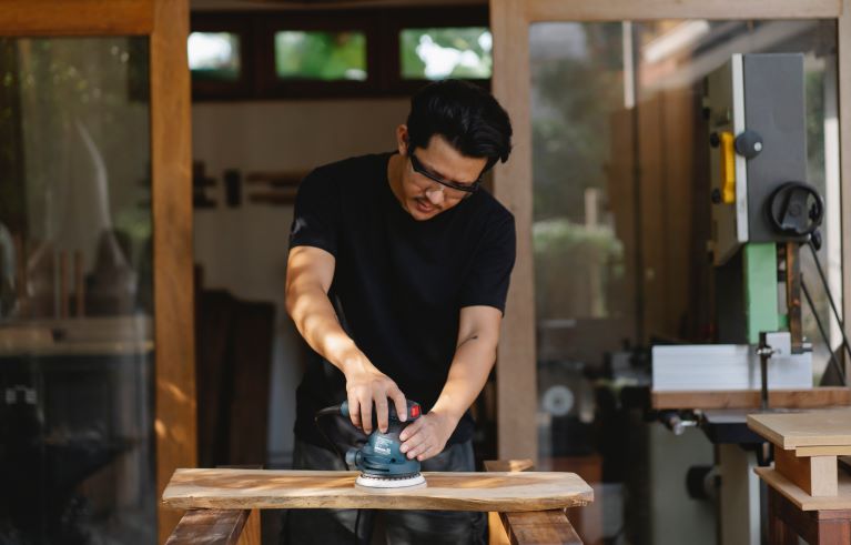 Middle aged man uses machine to buff wood