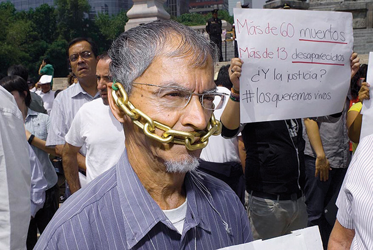 Journalists protest against rising violence during a march in Mexico. One journalist is wearing a chain, which is tied around his head and covering his mouth.
