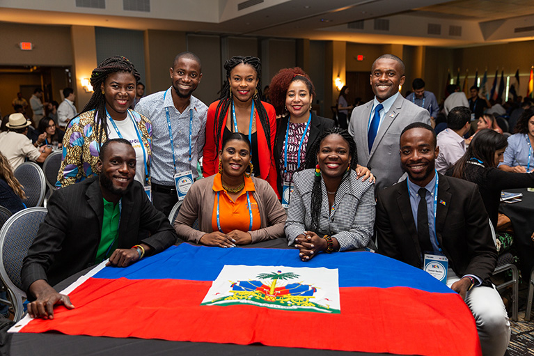 Photo of nine participants at a table in a conference hall. Haiti's flag is on the table.