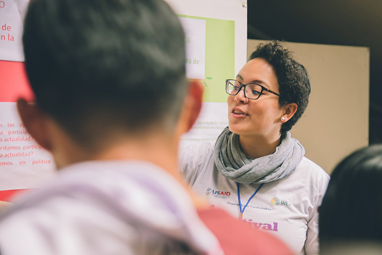 A young woman giving a presentation in front of a series of posters in Guatemala