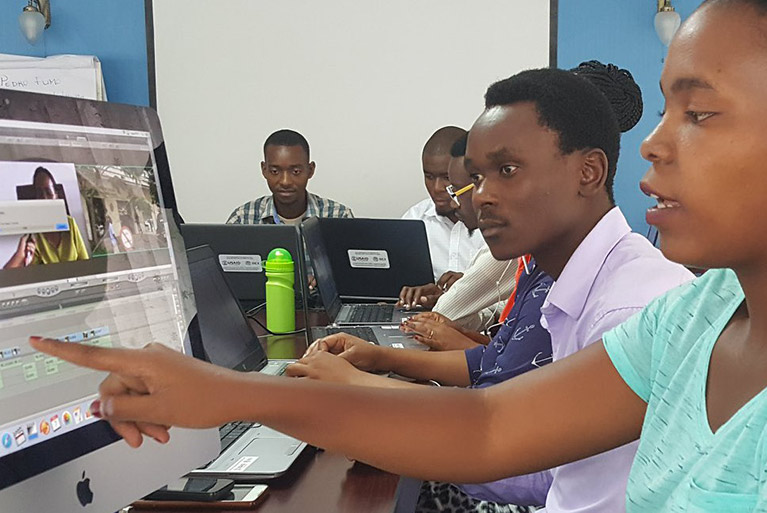 A woman pointing at a computer screen and talking to a colleague next to her while other participants work on laptops.