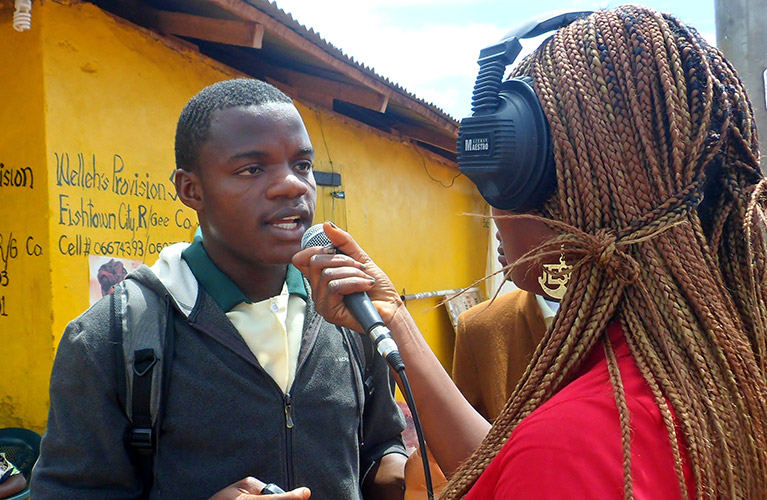 Photo of a journalist wearing headphones, holding a microphone, and conducting an interview.