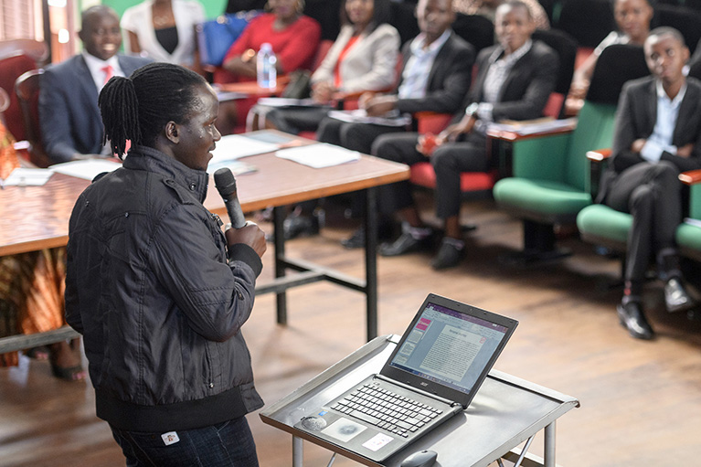 Photo of a young person speaking to an audience in an auditorium during a youth-led labor market assessment.