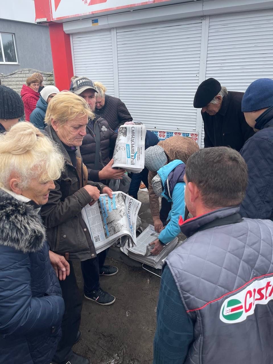 Photo of man and women gathered around a man distributing newspapers 