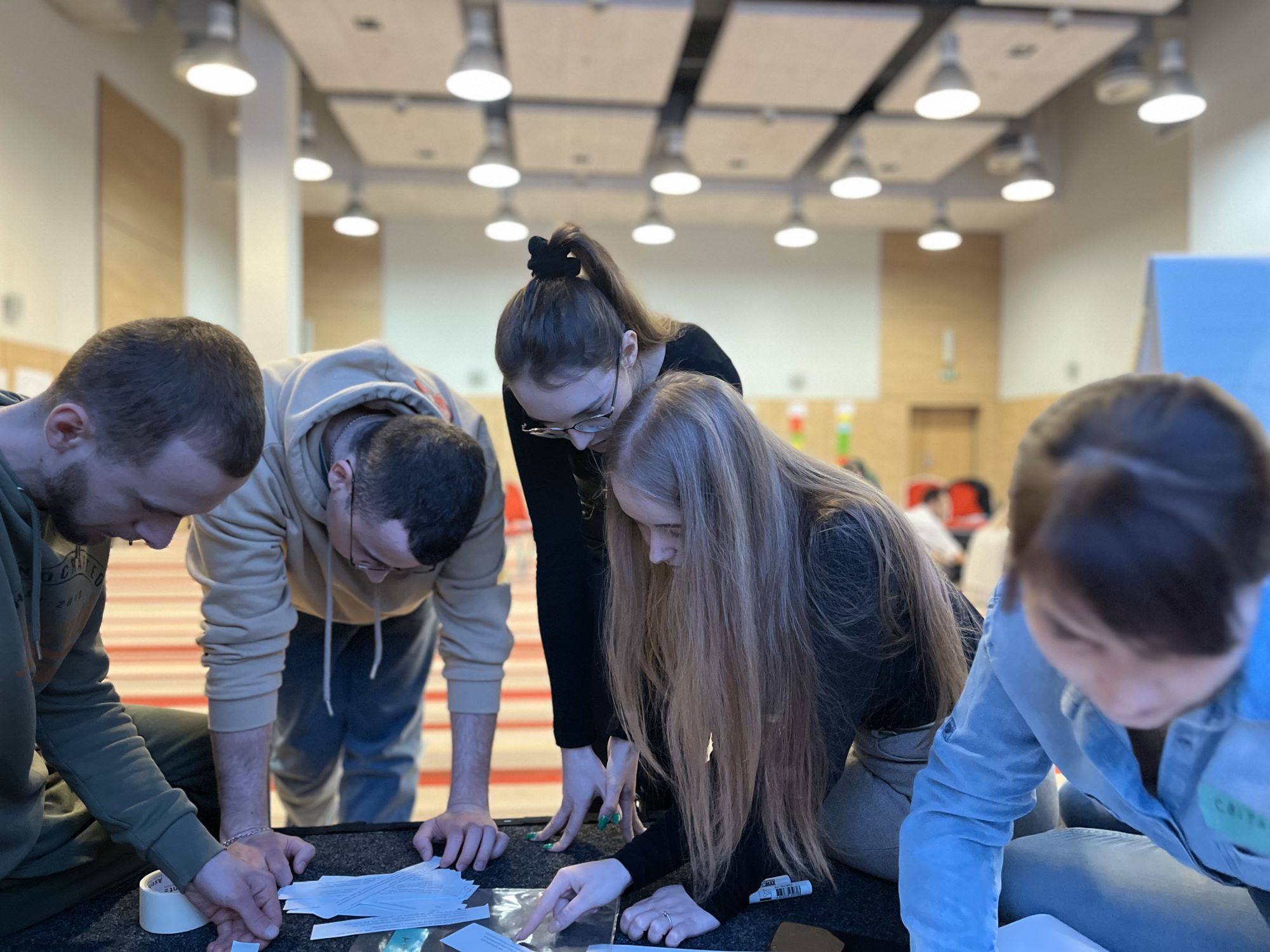 An image of male and female youth working together in a group. They are all looking  down at documents on a table. 