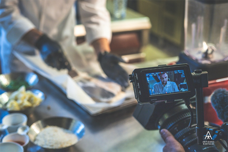 A video camera records a chef who is holding a spatula and preparing a dish.