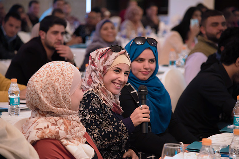 Three young women at an event in Jordan. One of the women is holding a microphone.