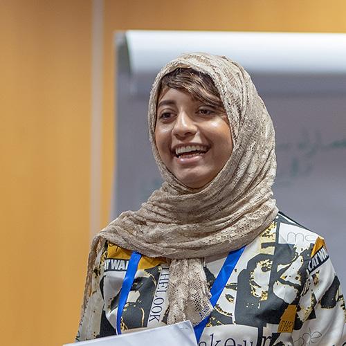 A smiling facilitator holding a piece of paper and standing in front of an easel pad.