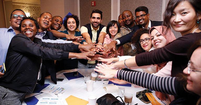 Fourteen people smiling and putting their hands in the middle of a table at a workshop